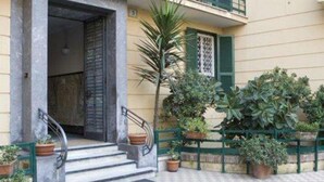 A two-story building with a balcony, a door with a metal gate, and potted plants. - A Casa di Penelope (Rome)