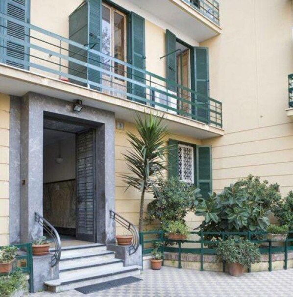 A two-story building with a balcony, a door with a metal gate, and potted plants. - A Casa di Penelope (Rome)