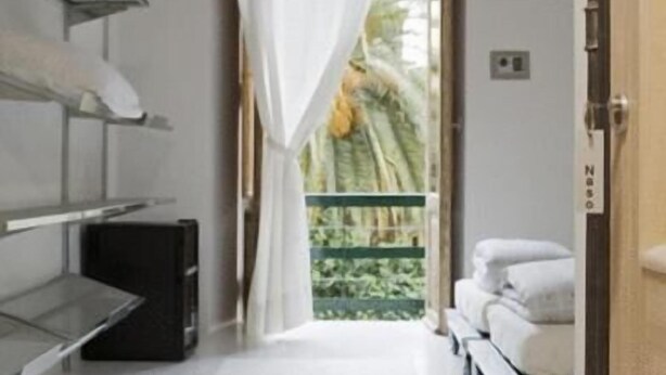 A hotel room with a bed, a desk with a computer, a window with curtains, and a view of greenery outside. - A Casa di Penelope (Rome)