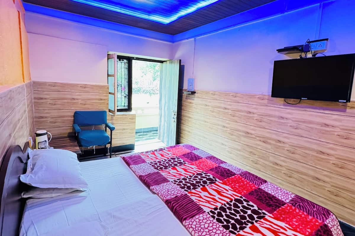 Une chambre d’hôtel moderne avec un plafond en bois, un grand lit recouvert d’une couverture à motifs, une chaise bleue et un téléviseur posé sur un meuble en bois.