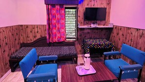 A room with a bed, a TV mounted on the wall, a table with chairs, and a window with curtains. - Shri Ganesh Hotel (Abu Road)