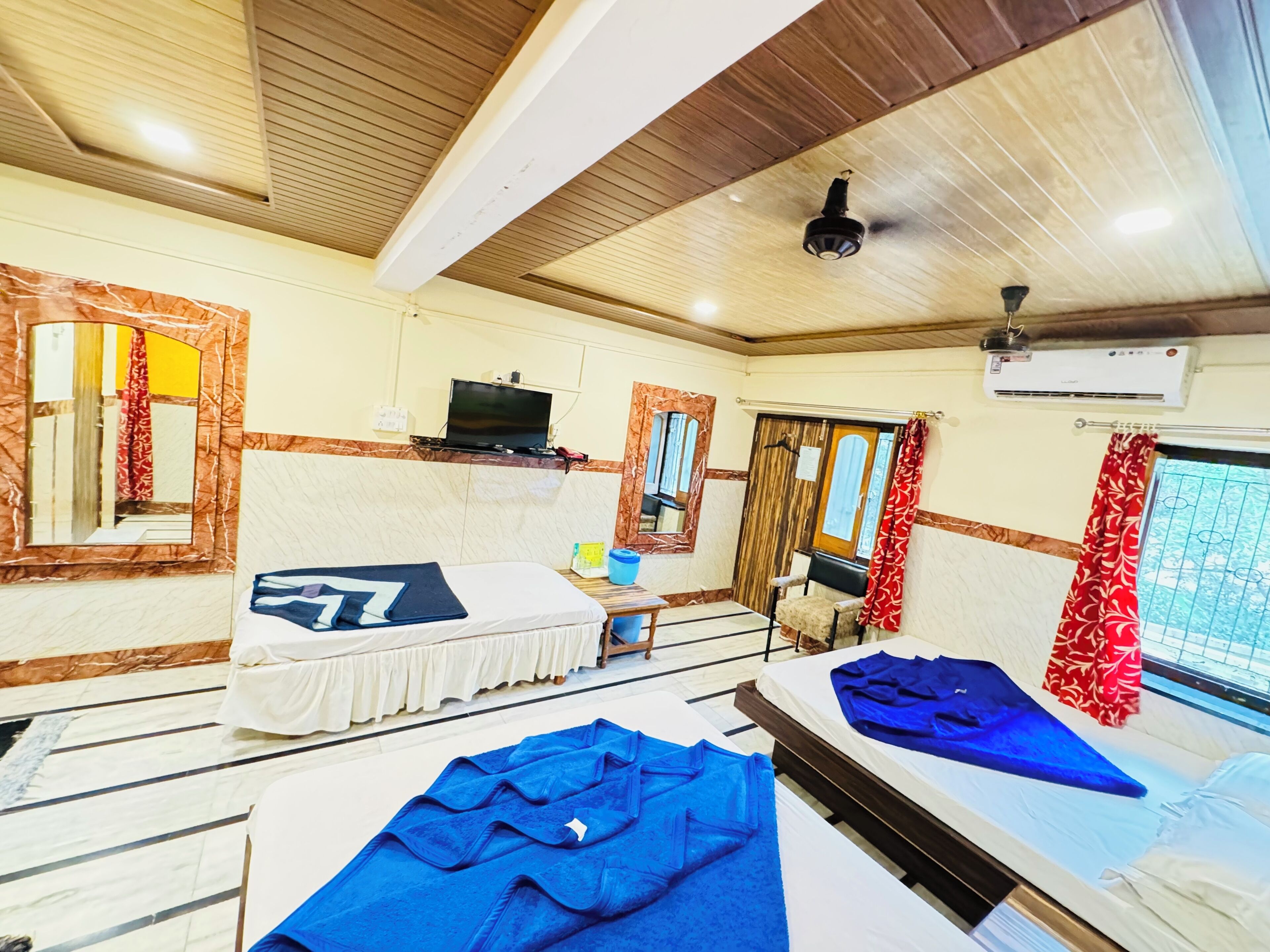 A hotel room with two beds, a desk, a TV, and an air conditioning unit.