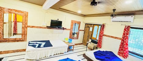 A hotel room with two beds, a desk, a TV, and an air conditioning unit.