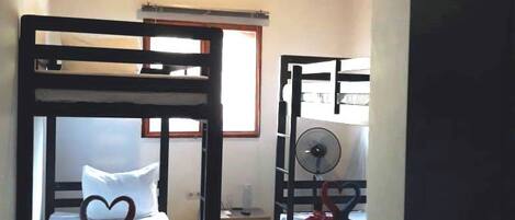 A room with bunk beds, a fan, and a wardrobe.