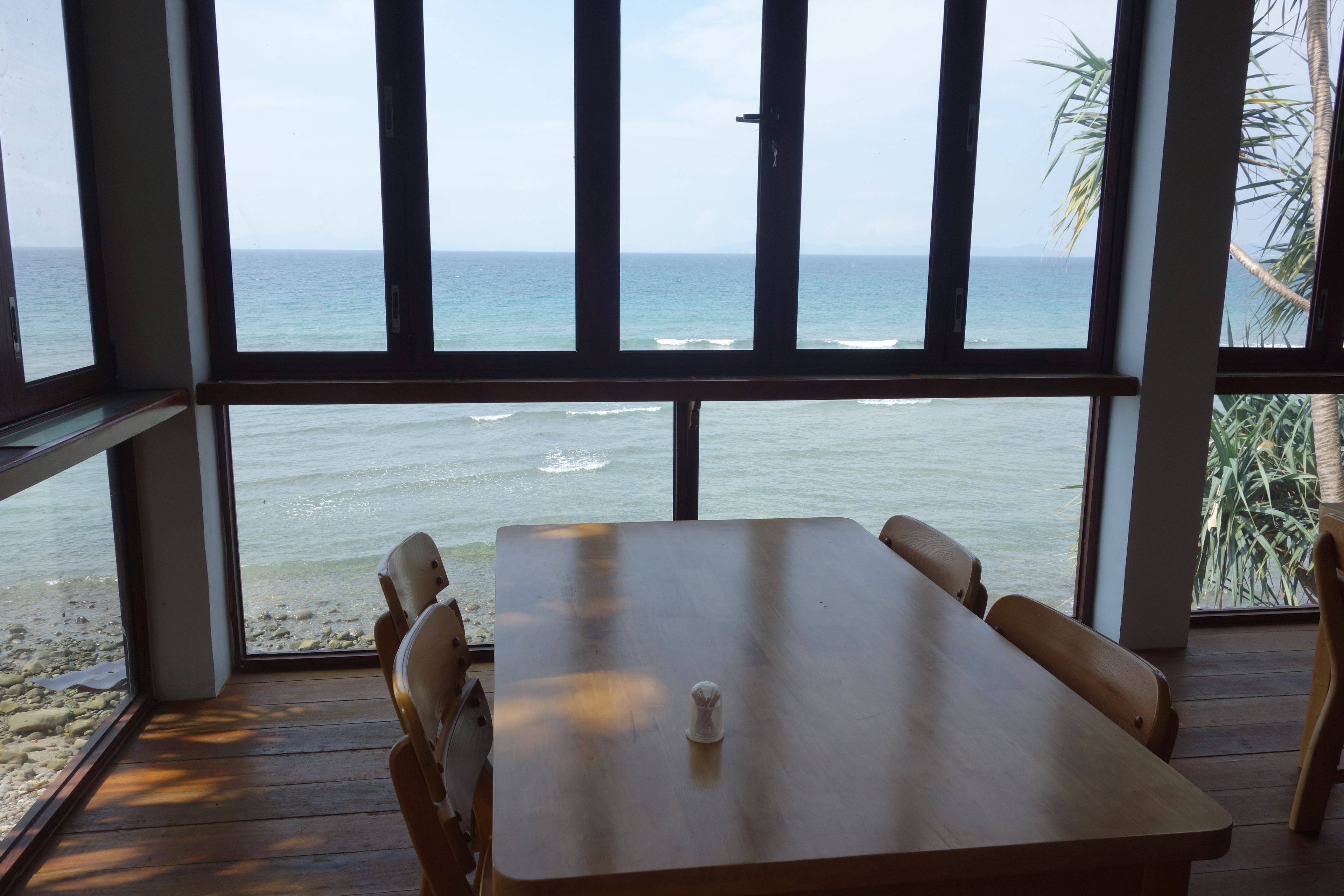 Una mesa de madera con cuatro sillas, un salero y vistas al océano a través de amplios ventanales.
