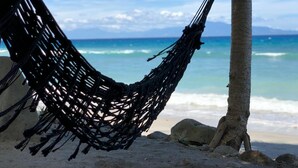 A hammock tied between two palm trees on a sandy beach with a view of the ocean.