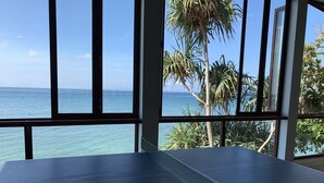 A ping pong table with a net in a room with large windows overlooking a body of water and palm trees.