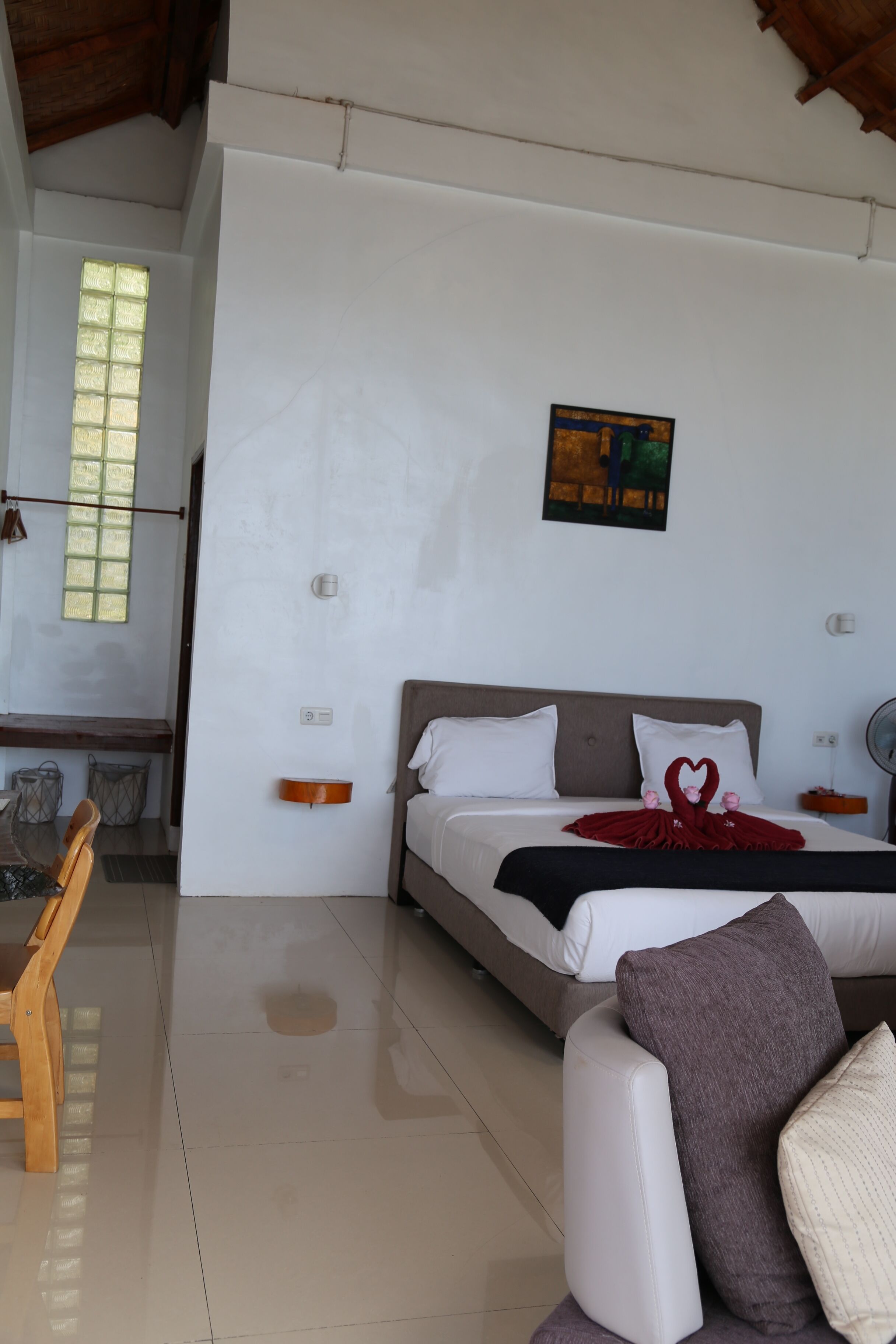 Una habitación de hotel con una cama, una silla de madera, una mesa y un cuadro en la pared.