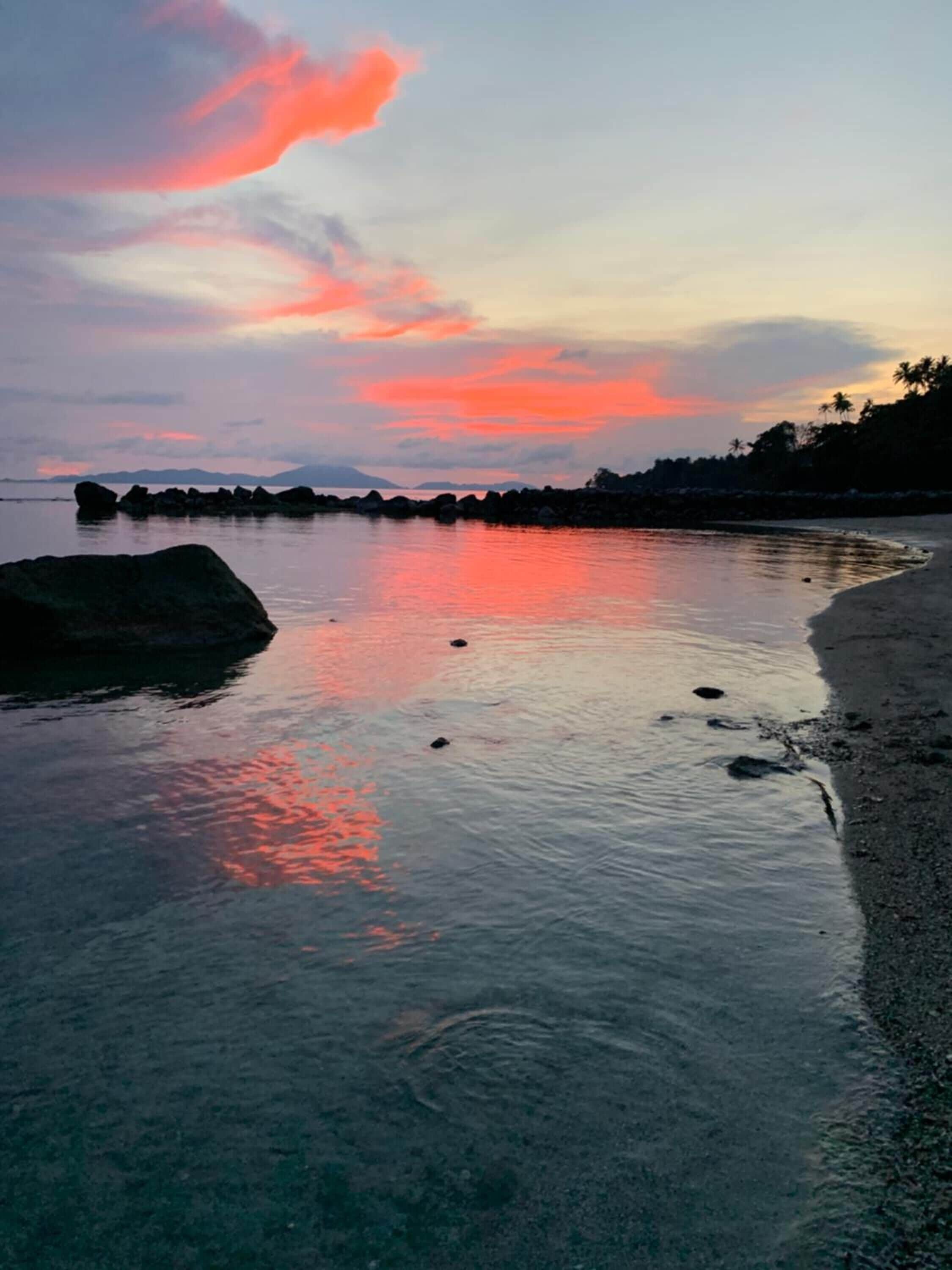 Una playa con aguas tranquilas reflejando un cielo al atardecer.