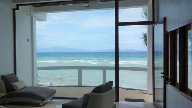 A modern room with a large sliding glass door leading to a balcony with a view of the ocean and mountains.