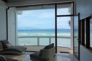 Una habitación moderna con un amplio ventanal corredera que da a un balcón con vistas al océano y las montañas.