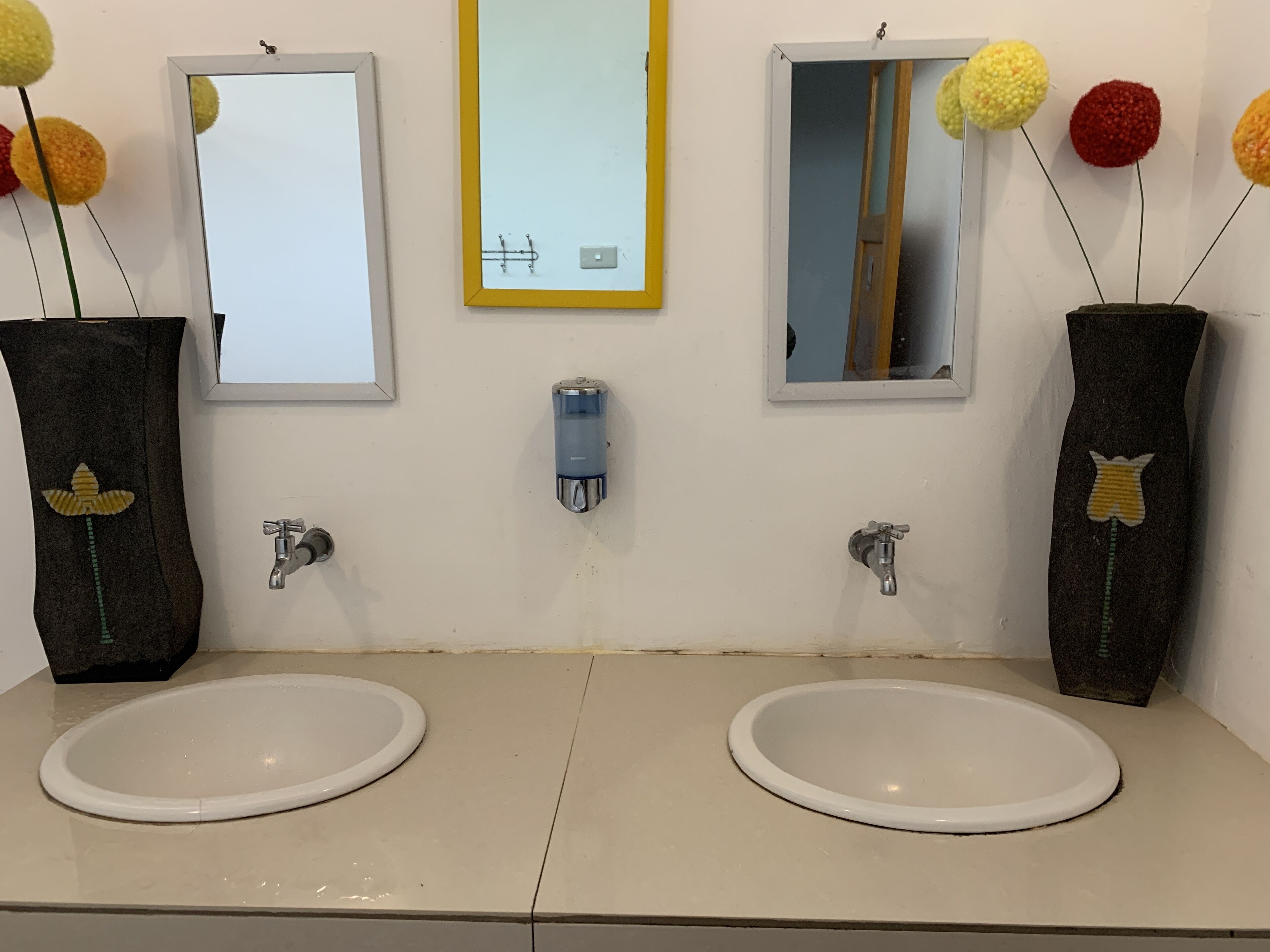 Un baño con dos lavamanos, espejos y jarrones decorativos con pompones.