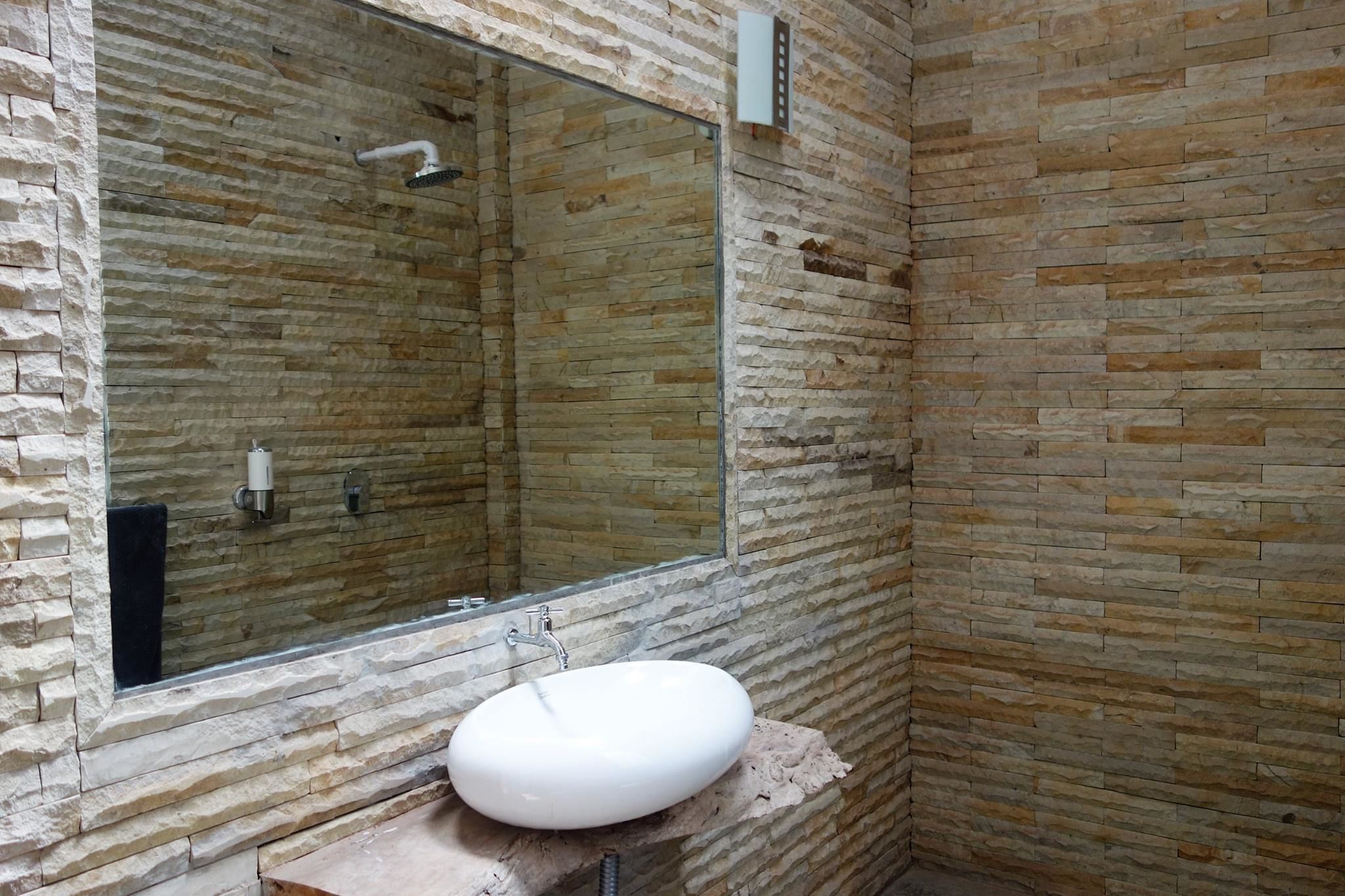 Une salle de bain avec un mur en pierre, un grand miroir et un lavabo blanc.