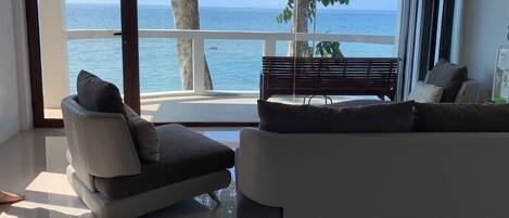 A modern bedroom with a large window overlooking the sea, a sofa, a bench, and a bed.
