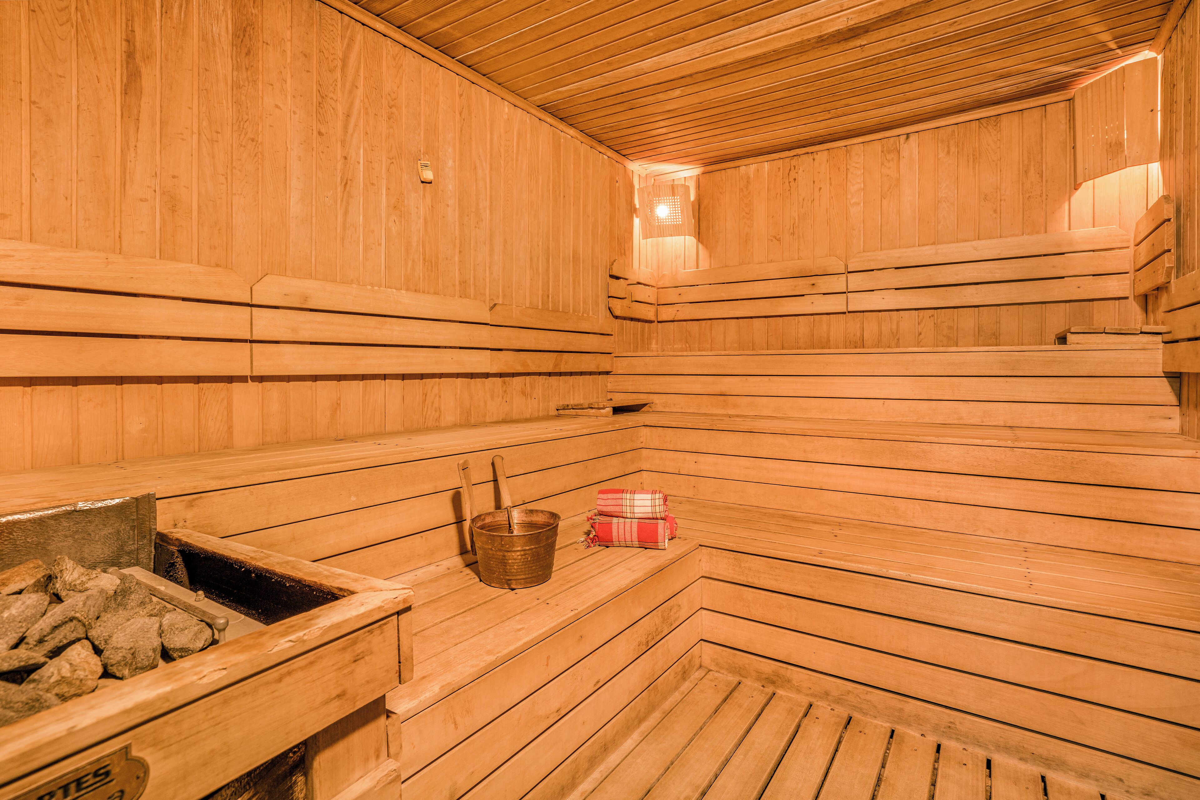 Una sauna de madera con bancos, un cubo y un pequeño calentador.
