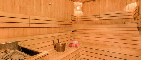 Una sauna de madera con bancos, un cubo y un pequeño calentador.