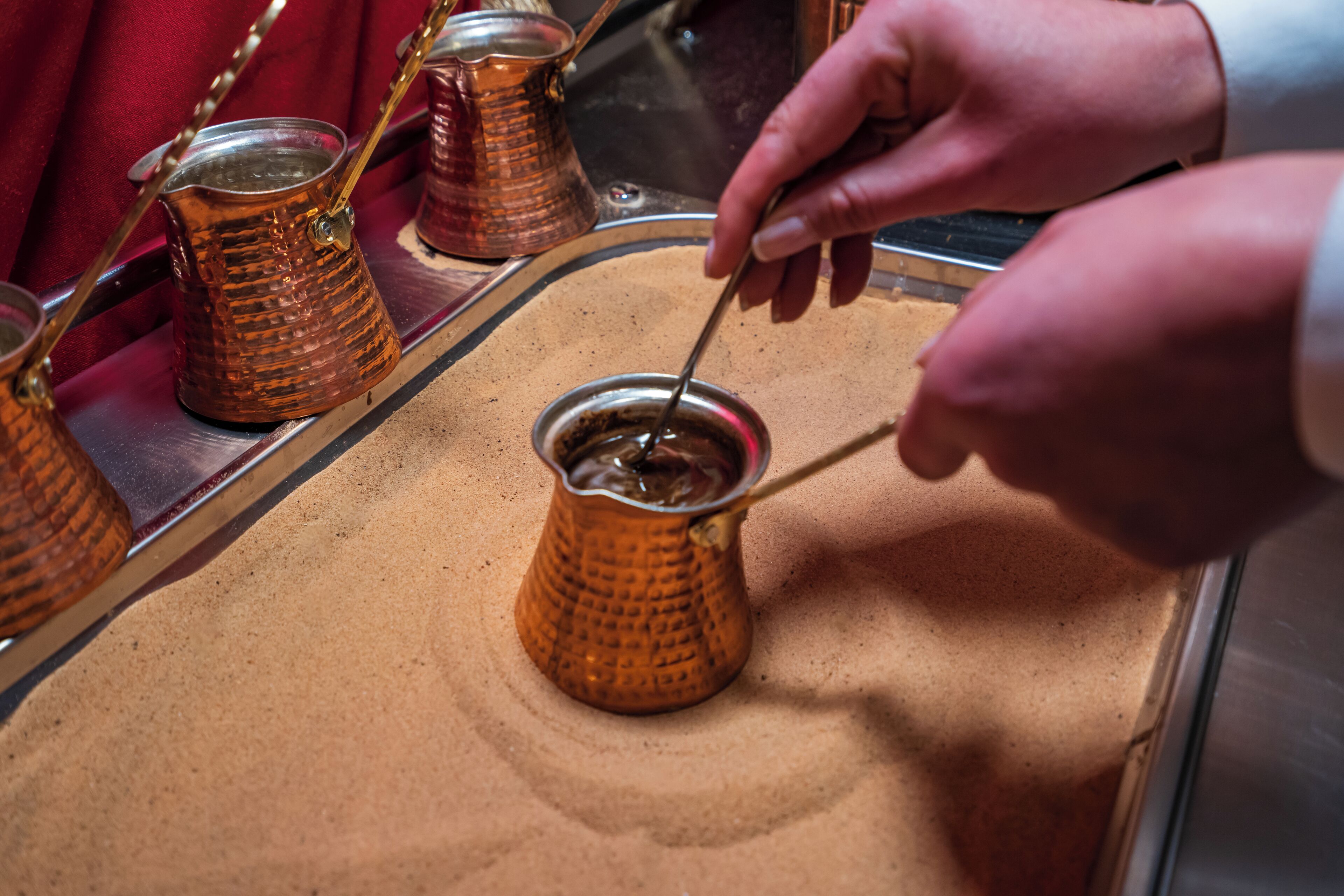 A hand stirring a small copper pot on a tray.
