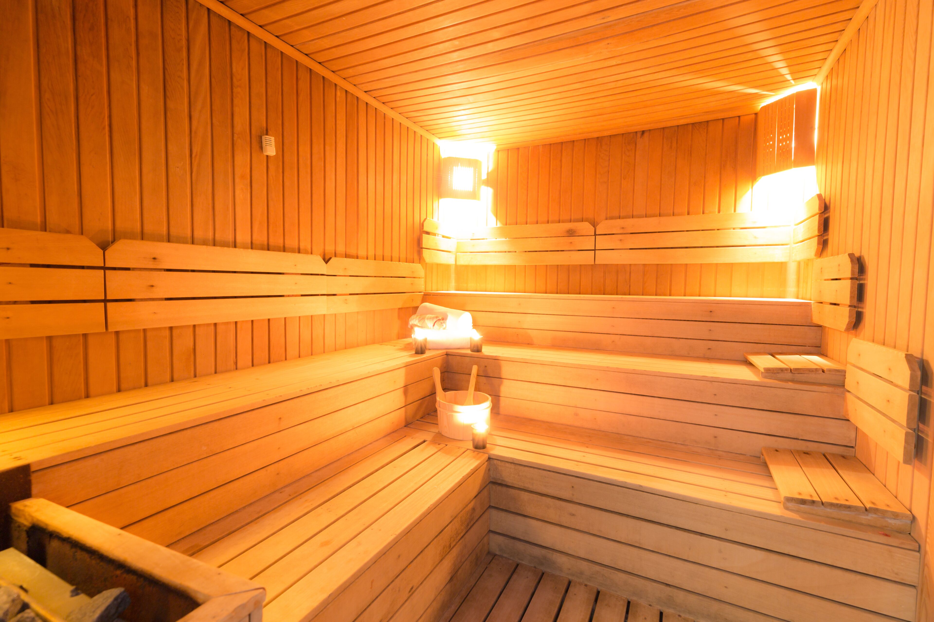 A sauna with wooden benches and benches, a light source, and a wall-mounted heater.