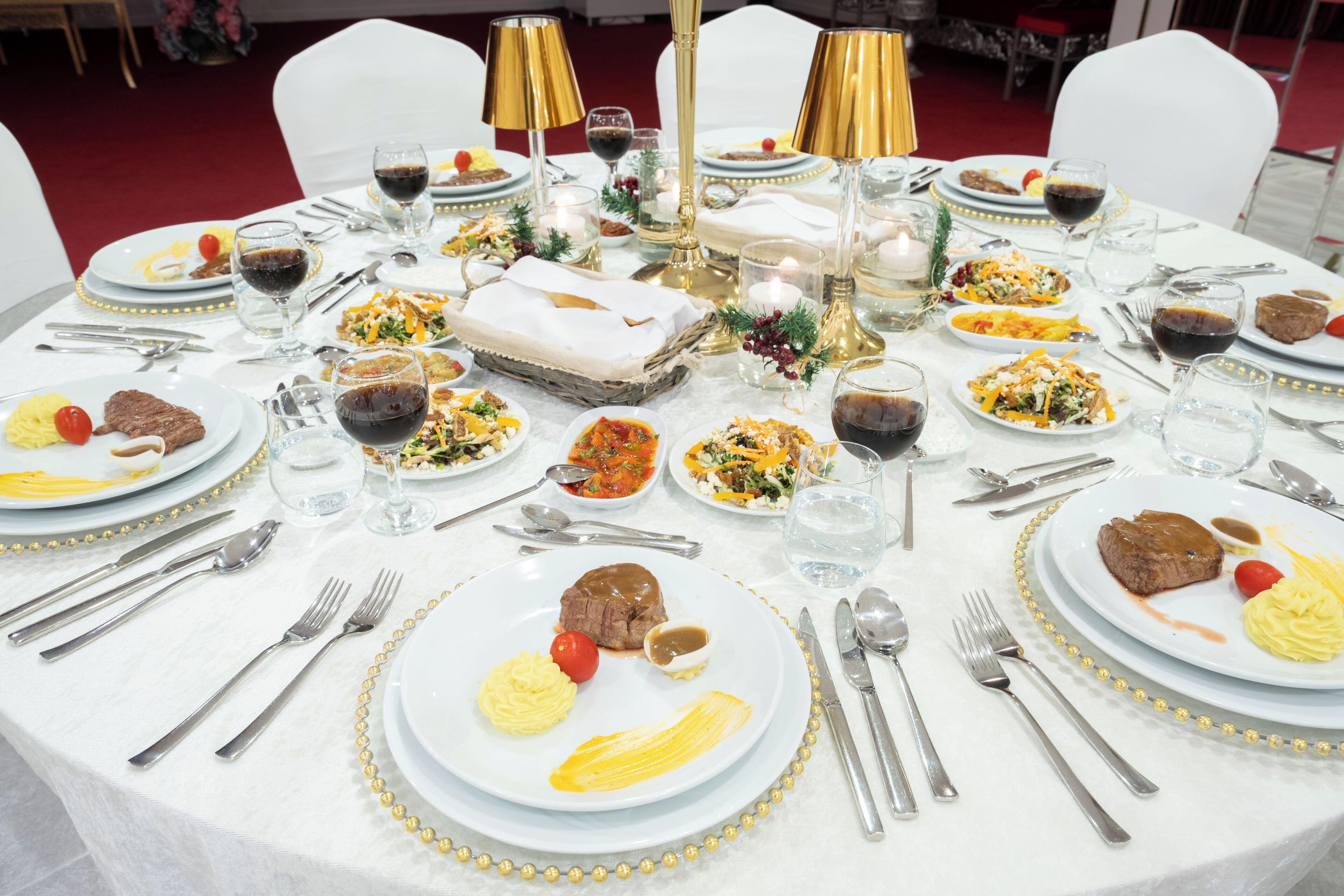 Een ronde eettafel gedekt met borden eten, glazen wijn en bestek.