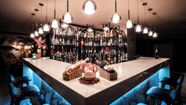 Zona de bar con una barra larga, varias lámparas colgantes y una amplia variedad de licores.