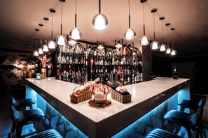 Un espace bar doté d’un long comptoir, de plusieurs luminaires suspendus et d’un bar bien garni.