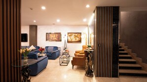 Un salón moderno con un sofá azul, una mesita con un jarrón de flores y una escalera que sube a un nivel superior.