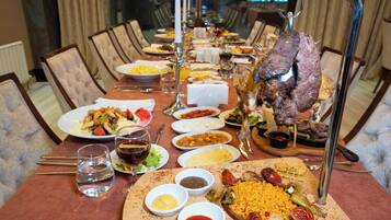 Une table à manger dressée avec différents plats, notamment un plat de viande rôtie en pièce maîtresse, plusieurs assiettes remplies de nourriture et plusieurs petits bols de sauces.