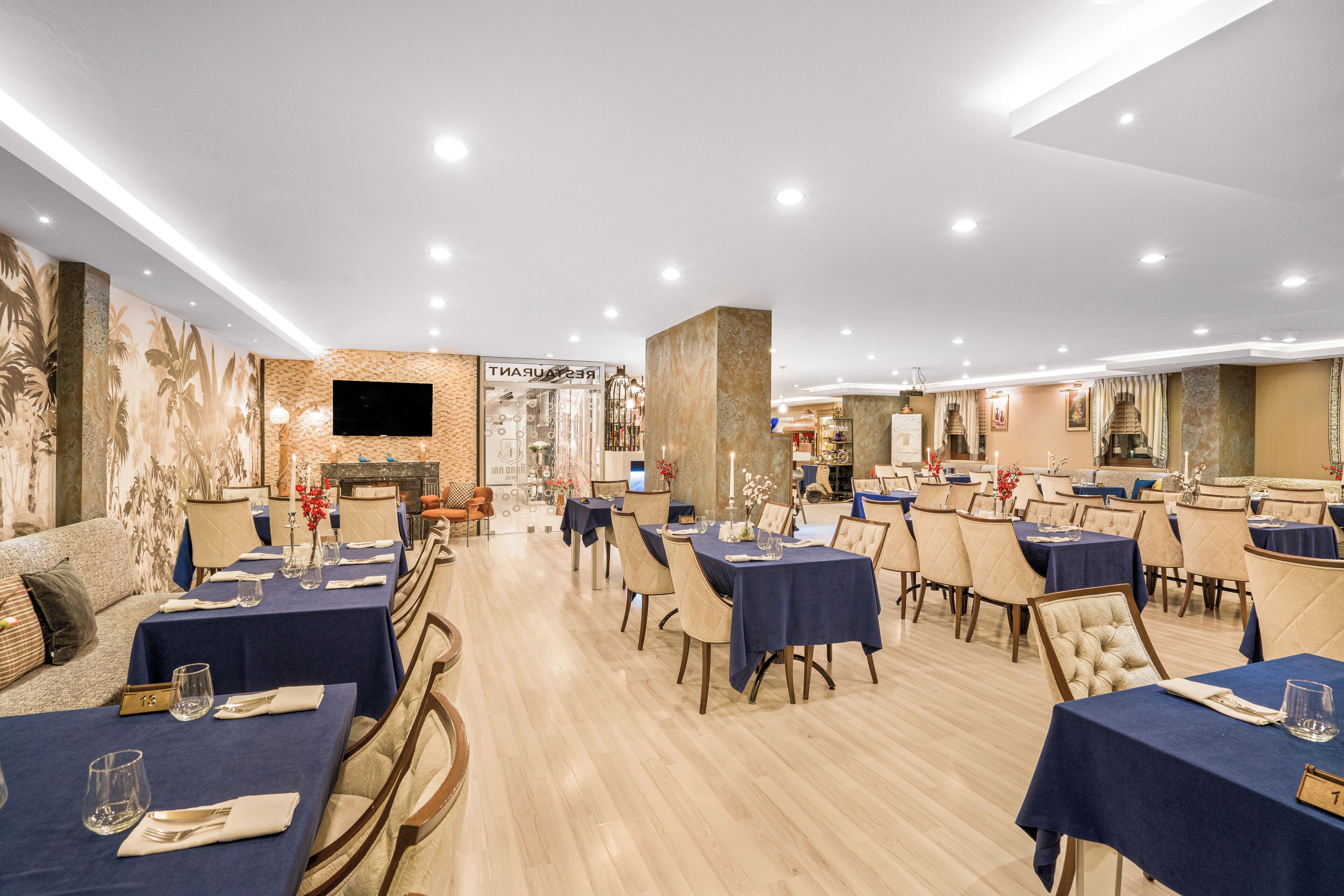 A restaurant with multiple tables set for dining, a bar area, and a television screen on the wall.