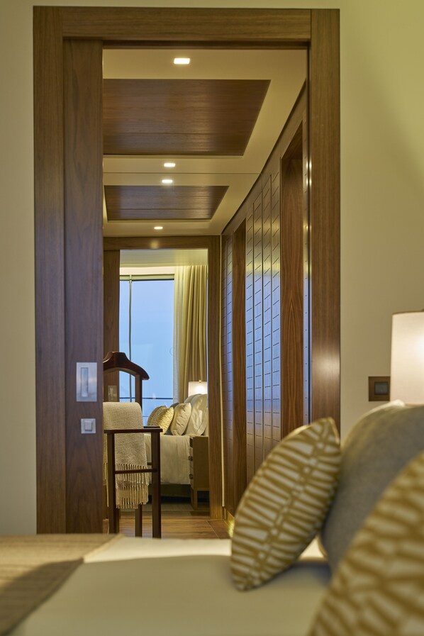 A hotel room with a wooden door, a bed with patterned pillows, a small table, and a chair.