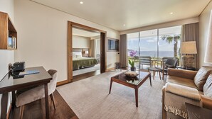 Ett modernt hotellrum med ett skrivbord, en soffa, ett soffbord och ett stort fönster med utsikt över havet.