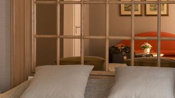 A hotel room with a large window, two pillows, a suitcase, and a vase with flowers on the bed.