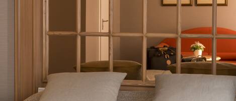 Habitación de hotel con una ventana grande, dos almohadas, una maleta y un jarrón con flores sobre la cama.
