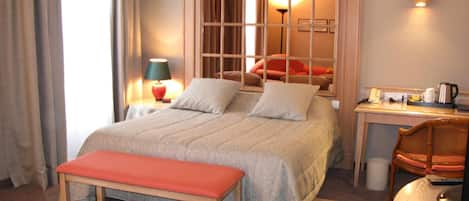 Habitación de hotel con una cama grande, un escritorio con una silla, una mesita pequeña y un banco.