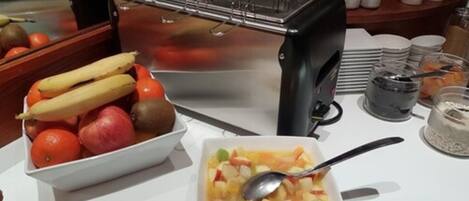 Montaje de bufé con un bol de fruta, una ensalada de frutas y un dispensador de bebidas.