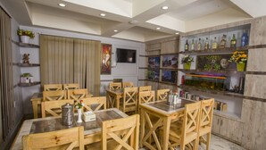 A restaurant with wooden tables and chairs, a bar area with shelves of bottles, and a television mounted on the wall.