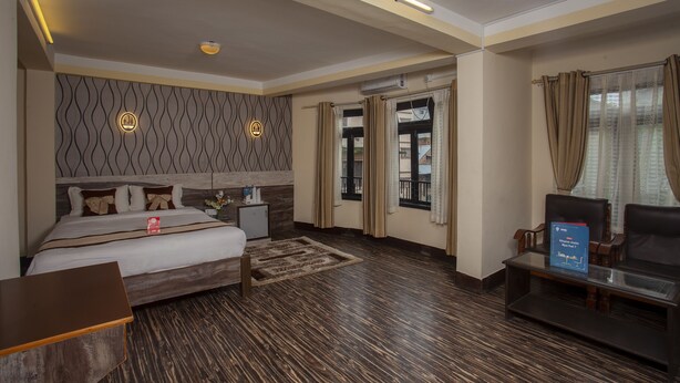 A hotel room with a large bed, a desk, a chair, and a small table. There is a window with curtains and a view of the outside.