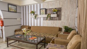 A living room with a sofa, armchairs, a glass coffee table, and decorative plants.