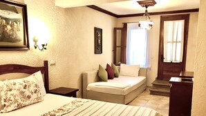 A bedroom with a bed, a sofa, a desk, and a staircase leading to another room. - Ada Bacchus Hotel (Bozcaada)