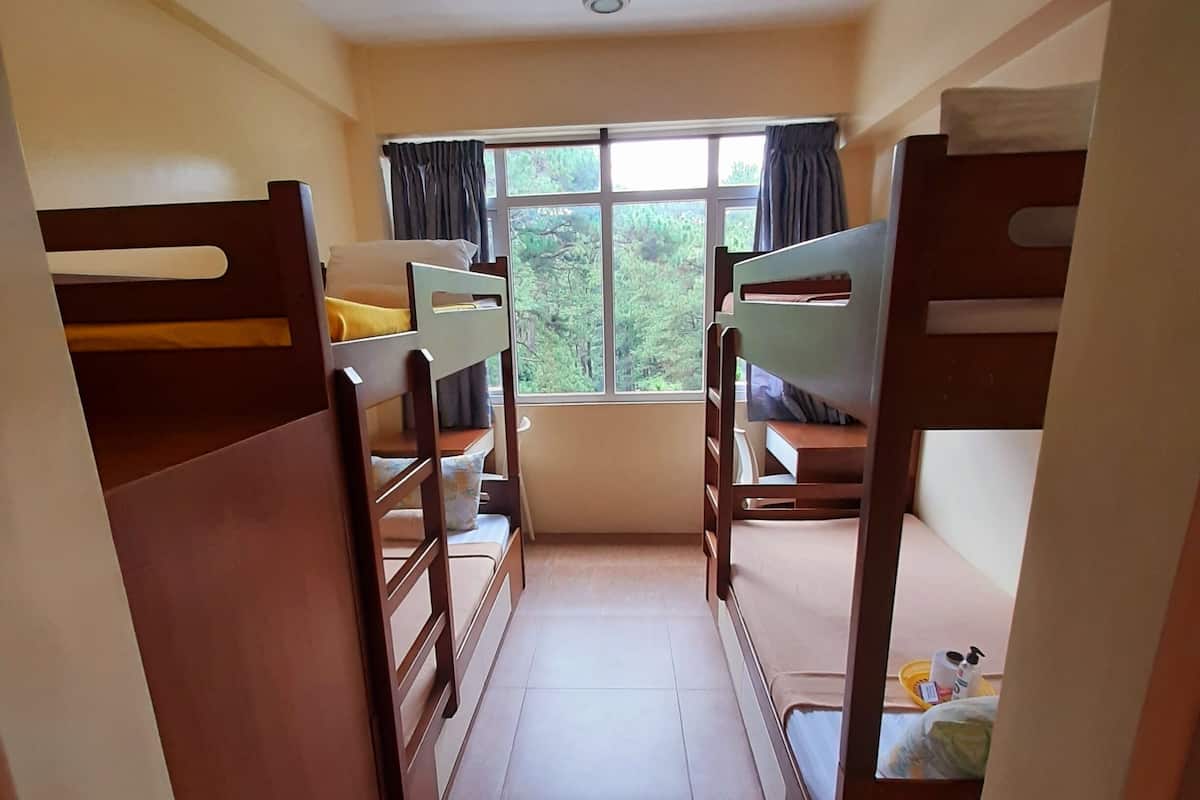 A narrow corridor with bunk beds on either side, leading to a window with a view of trees.