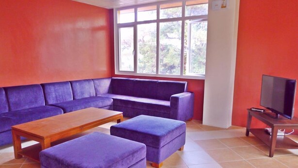 A living room with a purple sofa set, a wooden coffee table, and a television on a stand. - Arc Residences (Baguio)