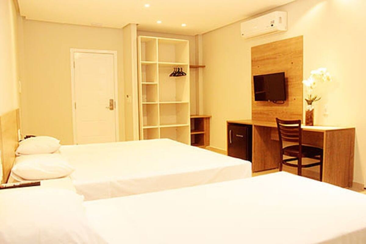 Habitación de hotel con dos camas, un escritorio, una silla, un televisor y un armario.