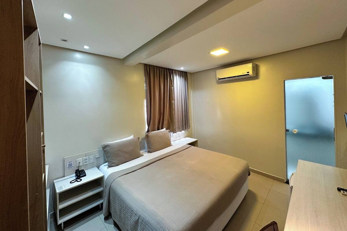 Una habitación de hotel con cama, mesita de noche y aire acondicionado.