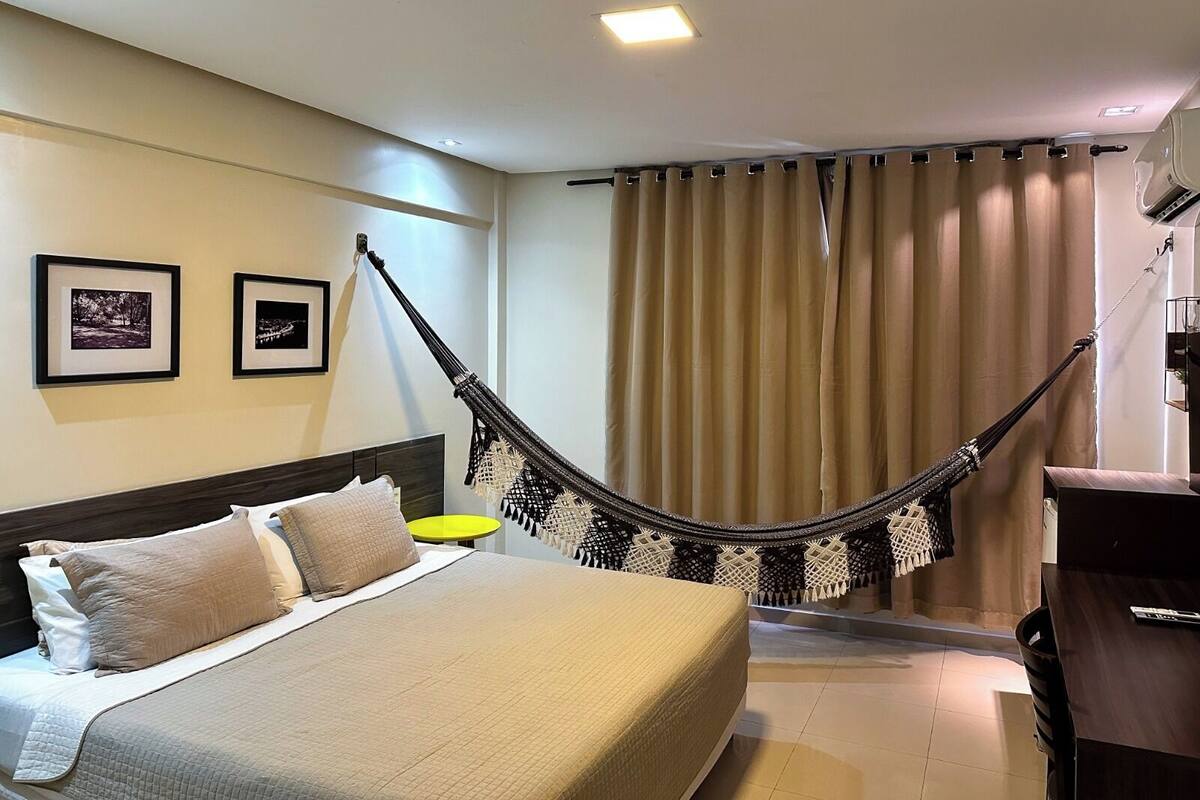 Una habitación de hotel con una cama, una hamaca, un escritorio y dos cuadros colgados en la pared.