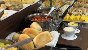 Un bufé con diversos alimentos, incluyendo pan, bollería y una variedad de platos en recipientes metálicos.