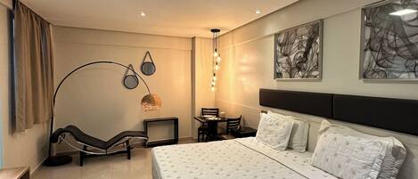 Una habitación de hotel moderna con una cama grande, un escritorio y una silla. Hay pinturas abstractas en las paredes y una lámpara en el techo.