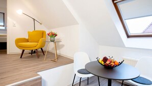Una habitación moderna y luminosa con una mesa de comedor, dos sillas, un sillón amarillo y una mesita auxiliar con un jarrón de flores.