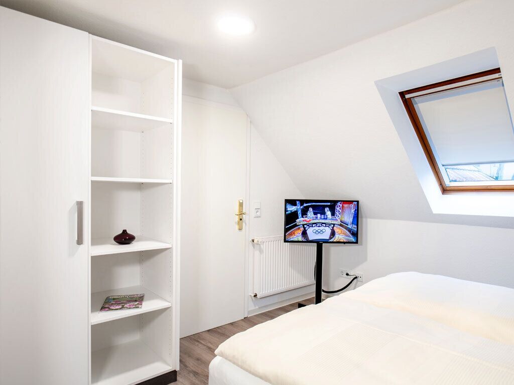 Camera da letto con un letto, un'armadio bianco, una televisione su un mobile e una finestra sul tetto.