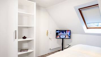 Camera da letto con un letto, un'armadio bianco, una televisione su un mobile e una finestra sul tetto.
