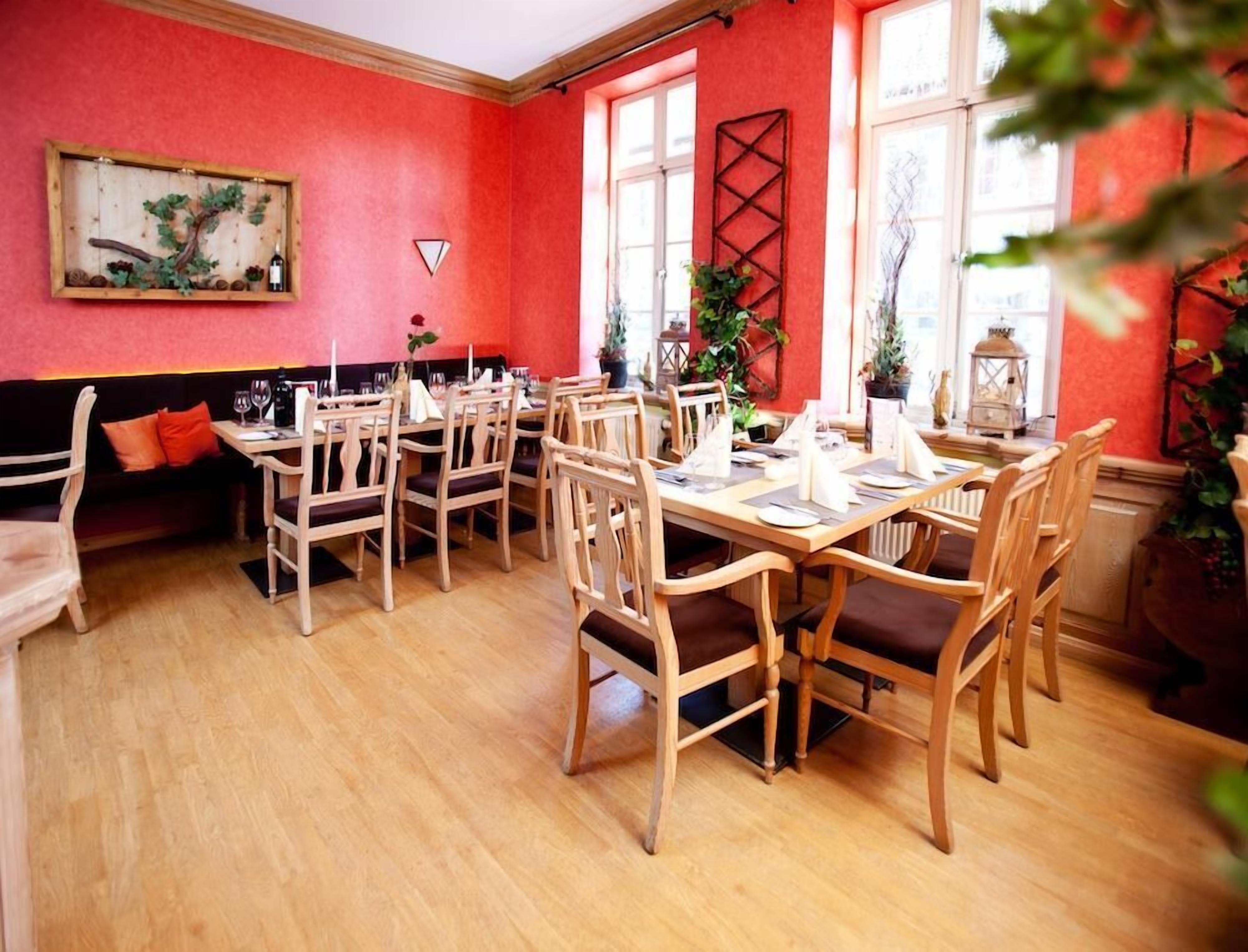 Un comedor con mesas y sillas de madera, paredes rojas y ventanas grandes.