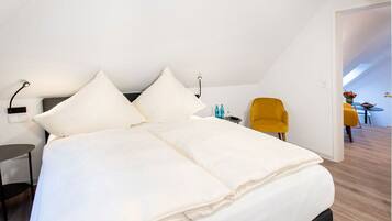 Un dormitorio moderno con una cama grande, una mesita de noche pequeña, una silla amarilla y vistas a un comedor.